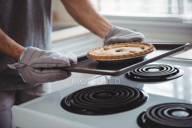 Средняя часть мужчины держит поднос свежеиспеченного пирога на кухне дома — стоковое фото