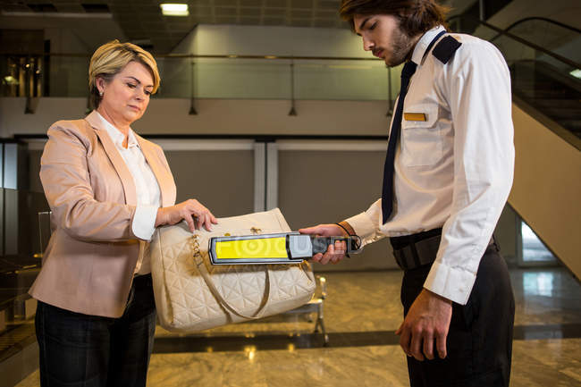 Oficial de seguridad del aeropuerto usando un detector de metales para revisar una bolsa en el aeropuerto - foto de stock