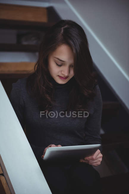 Женщина сидит на лестнице, используя цифровой планшет дома — стоковое фото