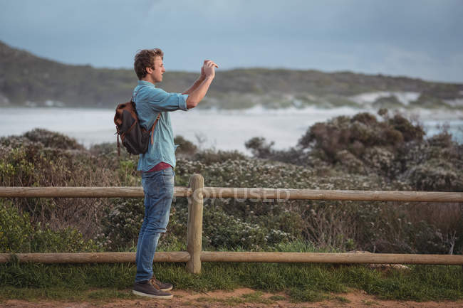 Чоловік стоїть за парканом фотографування за допомогою мобільного телефону — стокове фото