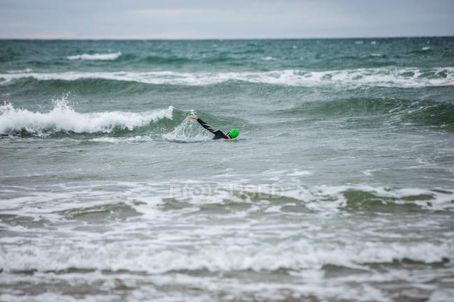 Человек в мокром костюме плавает в море на пляже — стоковое фото