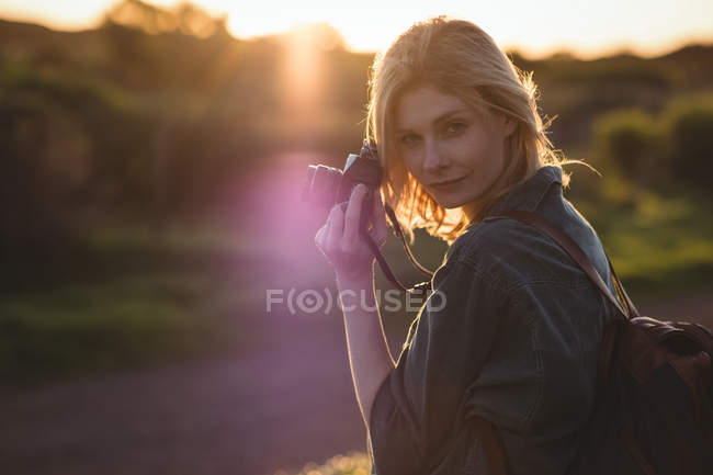 Retrato de una hermosa mujer sosteniendo una cámara digital en un día soleado - foto de stock