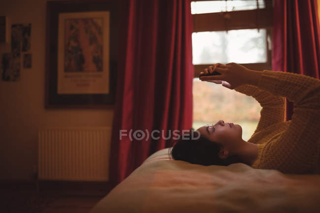 Женщина лежит и с помощью мобильного телефона на кровати в спальне на дому — стоковое фото