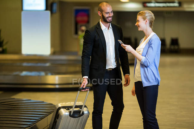 Улыбающаяся пара, взаимодействующая друг с другом в зоне ожидания терминала аэропорта — стоковое фото