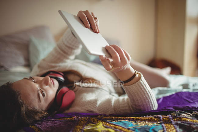 Femme utilisant une tablette numérique tout en prenant un café sur le lit à la maison — Photo de stock