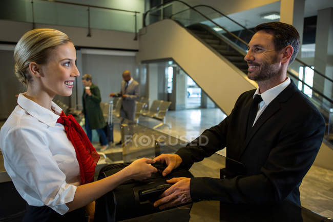 Female staff handing over luggage to businessman at airport terminal — Stock Photo