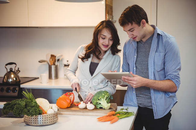 Пара с помощью цифрового планшета во время рубки овощей на кухне в домашних условиях — стоковое фото