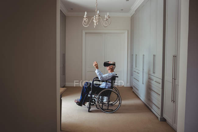 Старший мужчина сидит на инвалидной коляске и использует гарнитуру виртуальной реальности дома — стоковое фото