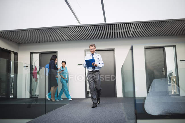 Médico mirando el informe médico mientras camina en el pasillo del hospital - foto de stock