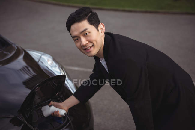 Hombre sonriente cargando coche en la estación de carga del vehículo eléctrico - foto de stock