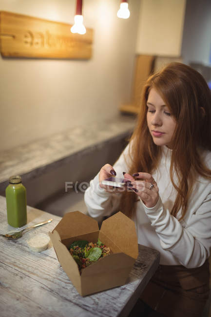 Женщина фотографирует салат на мобильный телефон в ресторане — стоковое фото