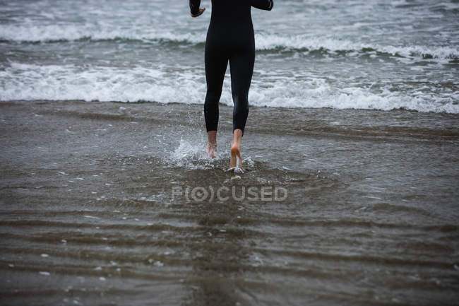 Низька секція спортсмена у вологому костюмі, що йде в бік моря — стокове фото