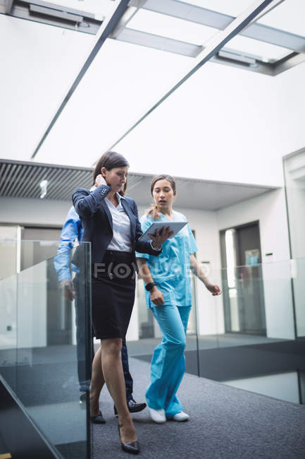 Доктор і медсестра обговорюють цифровий планшет під час прогулянки в лікарняному коридорі — стокове фото