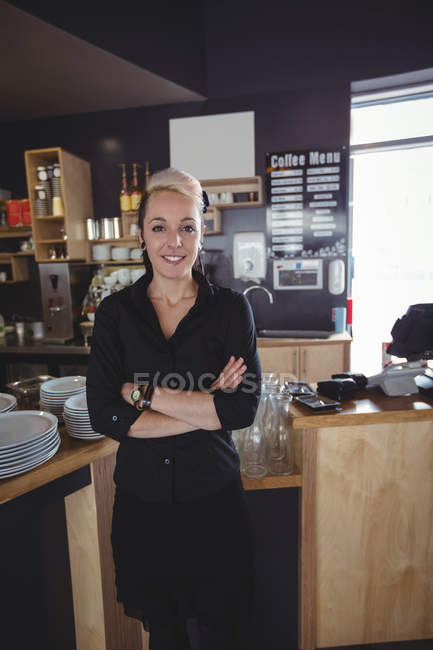 Retrato de camarera de pie con los brazos cruzados en la cafetería - foto de stock