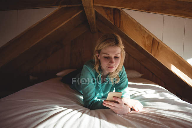 Bella donna sdraiata sul letto e utilizzando il telefono cellulare in camera da letto a casa — Foto stock