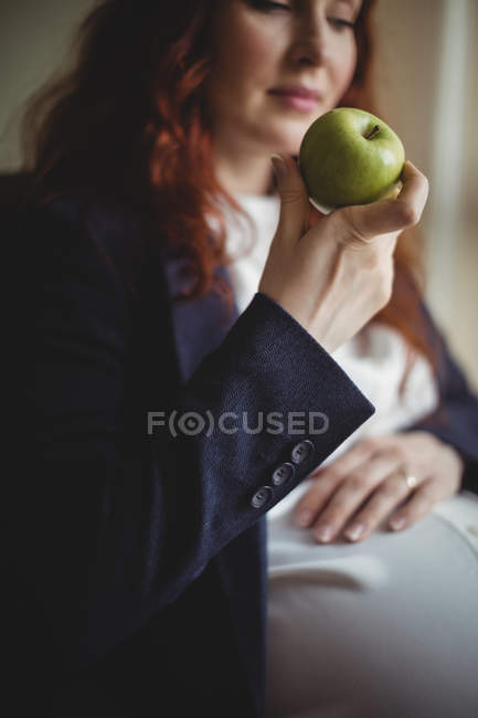 Embarazada mujer de negocios sosteniendo una manzana en el cargo - foto de stock