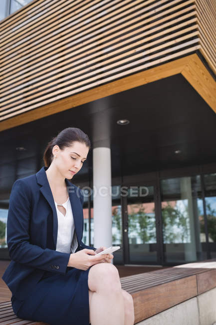 Бизнесмен, сидящая снаружи офисного здания и пользующаяся мобильным телефоном — стоковое фото