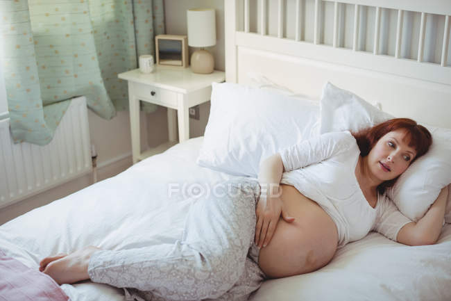 Задумчивая беременная женщина отдыхает на кровати в спальне — стоковое фото