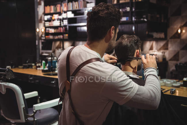 Homem recebendo cabelo aparado por cabeleireiro com tesoura na barbearia — Fotografia de Stock