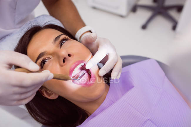 Крупный план стоматолога, осматривающего женские зубы с зеркалом во рту — стоковое фото