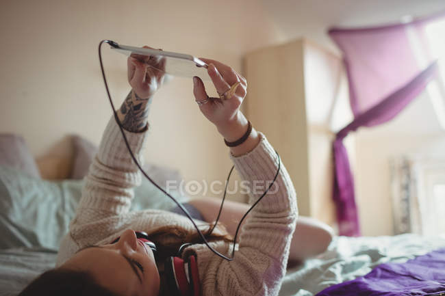 Femme utilisant une tablette numérique sur le lit à la maison — Photo de stock