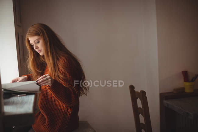Redhead woman reading book at window in restaurant — Stock Photo