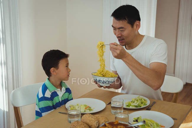 Père servant de la nourriture à son fils sur la table à manger à la maison — Photo de stock