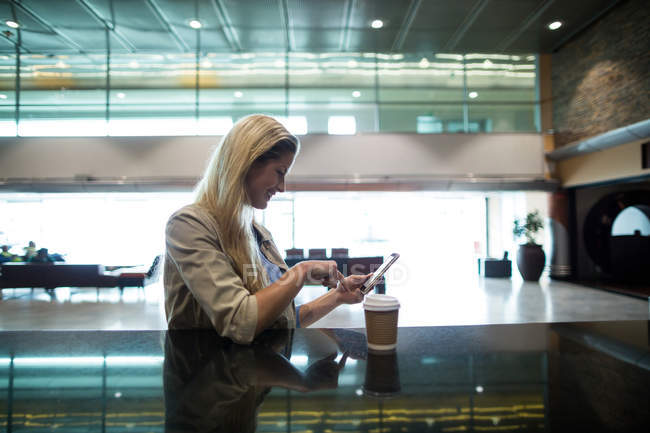 Mujer sonriente usando teléfono móvil en la sala de espera en la terminal del aeropuerto - foto de stock