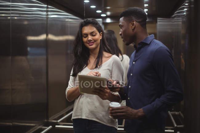 Businessman and a colleague discussing over digital tablet and mobile phone in office elevator — Stock Photo