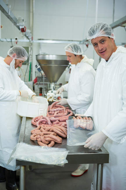 Açougues embalando e processando salsichas cruas na fábrica de carne — Fotografia de Stock