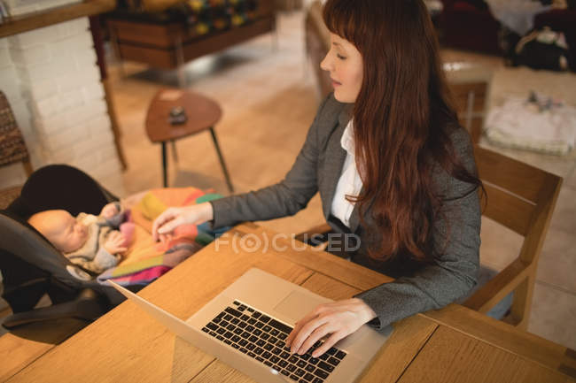 Mother using laptop while taking care of newborn baby at home — Stock Photo