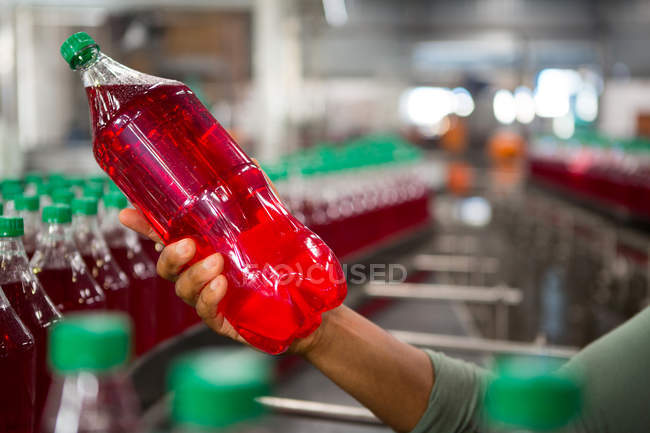 Обрезанная рука работника, держащего бутылку красного сока на заводе — стоковое фото