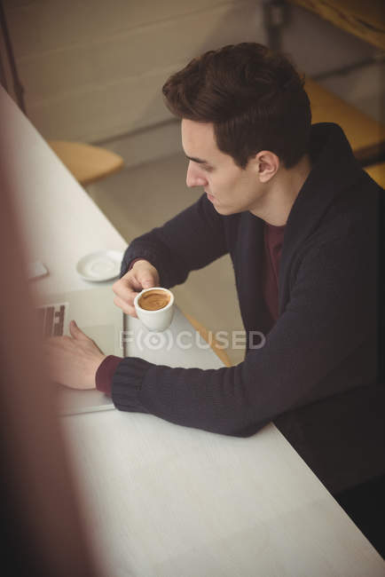 Homem usando laptop enquanto toma café na cafeteria — Fotografia de Stock