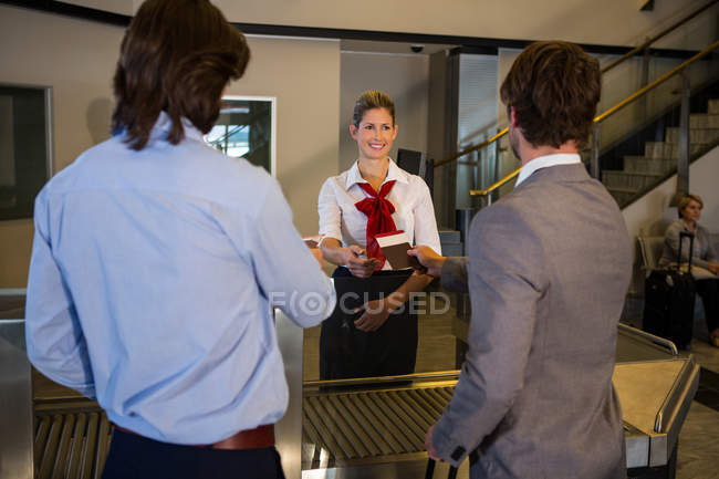 Pessoal feminino que verifica o cartão de embarque dos passageiros no balcão de check-in no aeroporto — Fotografia de Stock