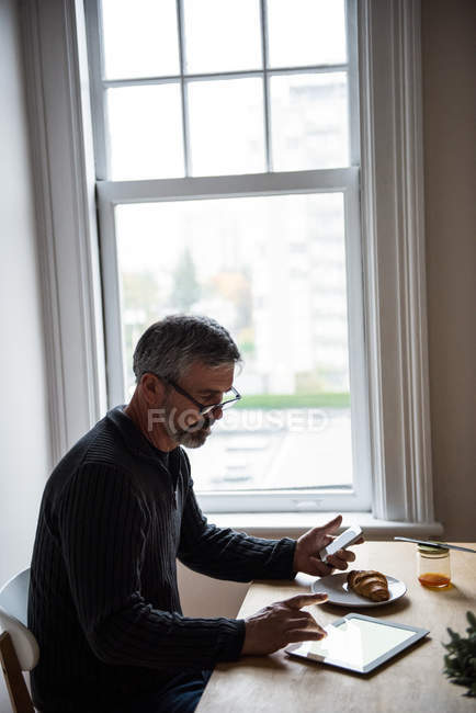 Man using digital tablet and mobile phone in living room at home — Stock Photo