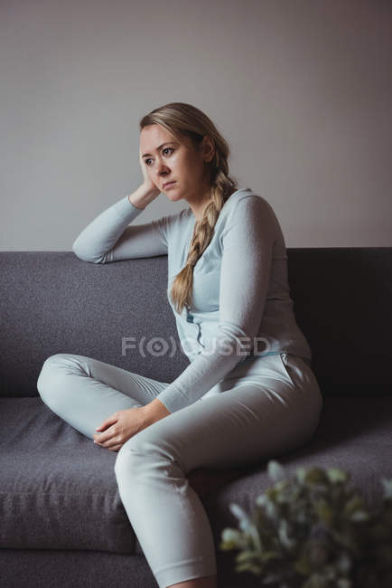 Tensed woman sitting on sofa in living room at home — Stock Photo
