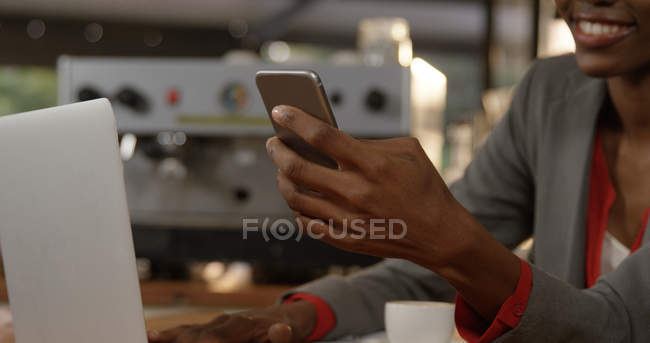 Frau benutzt Mobiltelefon während sie Laptop im Büro benutzt — Stockfoto
