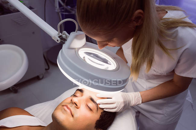 Médica examinando o rosto masculino para tratamento cosmético na clínica — Fotografia de Stock