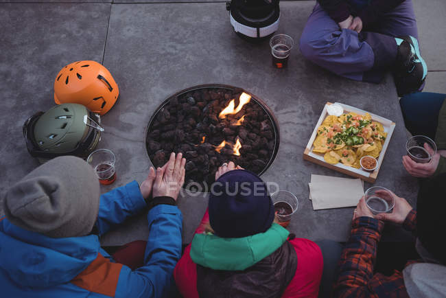 Group of skiers rubbing hands near fireplace in ski resort — Stock Photo