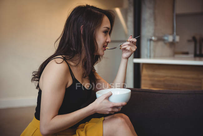 Frau sitzt auf Sofa und isst Frühstücksflocken im heimischen Wohnzimmer — Stockfoto