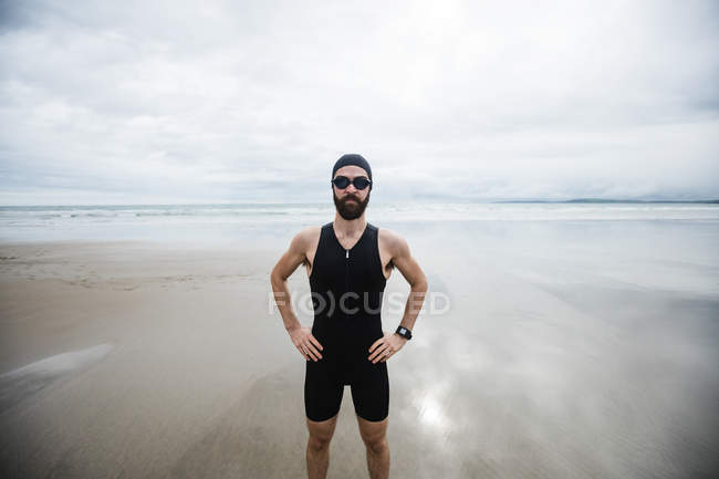 Sportler mit Schwimmbrille steht mit Hand auf Hüfte am Strand — Stockfoto