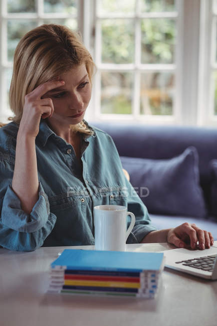 Femme tendue utilisant un ordinateur portable dans le salon à la maison — Photo de stock