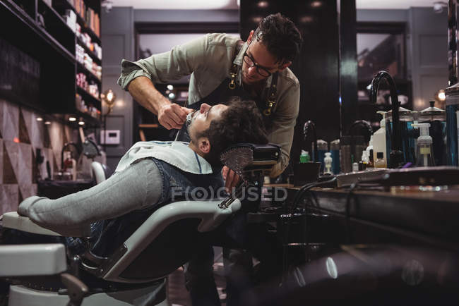 Hombre conseguir barba afeitado por peluquero con maquinilla de afeitar en peluquería - foto de stock