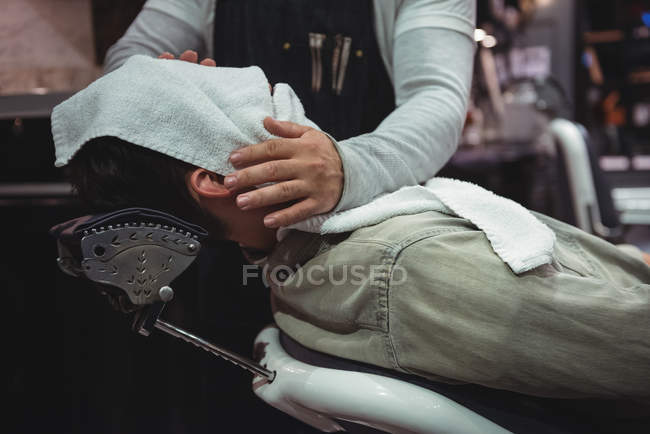 Mid section on barber wiping client face with hot towel in barber shop — Stock Photo
