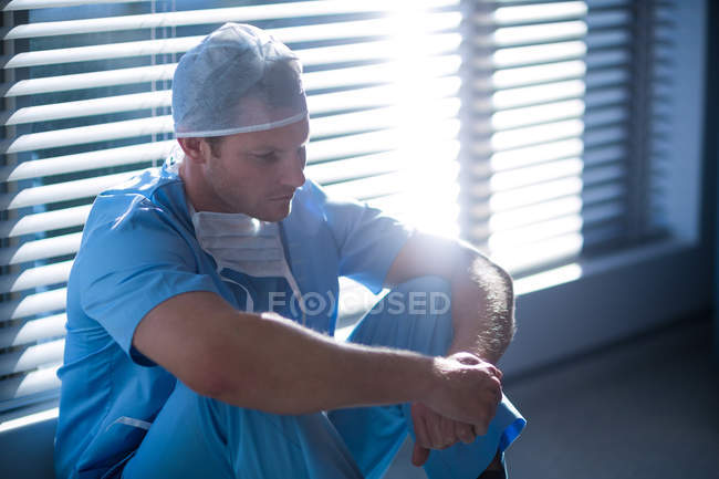 Enfermera masculina ensangrentada sentada en pasillo del hospital - foto de stock