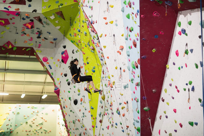 Mujer practicando escalada en roca en muro de escalada artificial en gimnasio - foto de stock