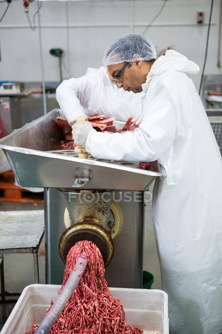 Butchers placing meat in mincing machine at meat factory — Stock Photo