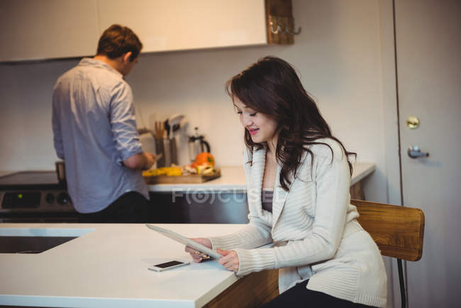 Woman using digital tablet while man working in background at kitchen — Stock Photo