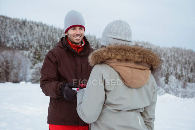 Жінка дарує подарунок усміхненому чоловікові на снігу покритій горі — стокове фото