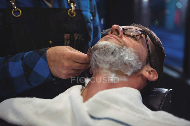 Customer getting beard shaved with razor in barber shop — Stock Photo